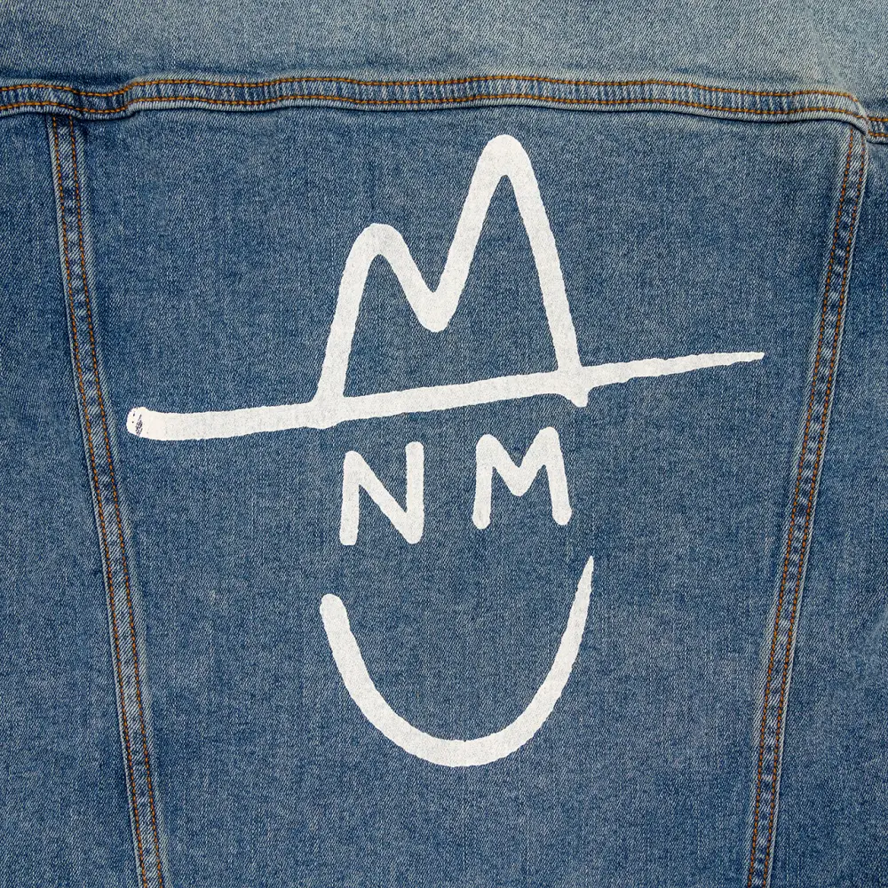Denim jacket with a white stylized smiley face logo featuring ’NM’ initials.