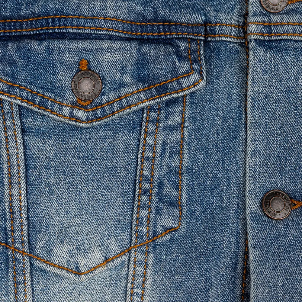 Denim jacket pocket with metal buttons and contrast stitching.