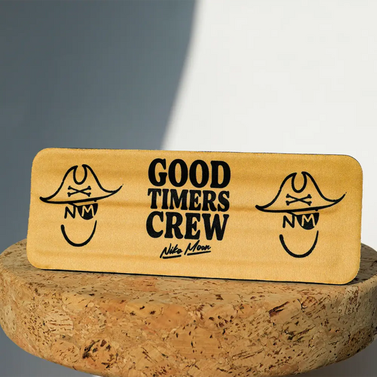 A rectangular wooden plaque with a light golden-brown finish, featuring black engraved pirate-themed logos and the text ’good timers crew’ along with the signature ’nike moon.’