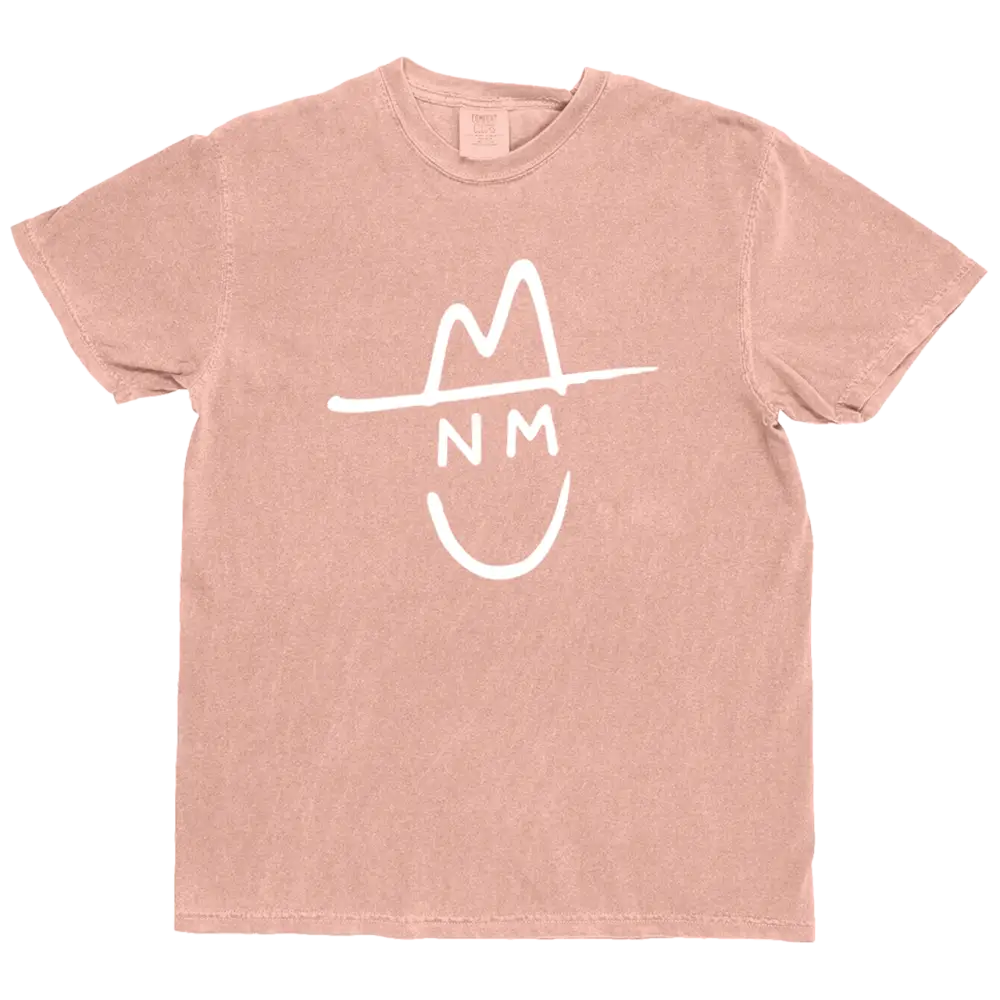 A soft blush pink cotton t-shirt featuring a white stylized graphic of a smiling face wearing a hat with ’nm’ printed below.