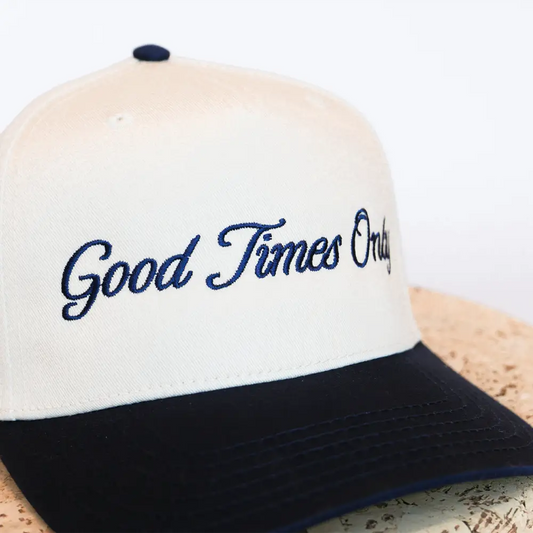 Cream-colored baseball cap with navy blue brim and embroidered ’good times only’ in cursive script.