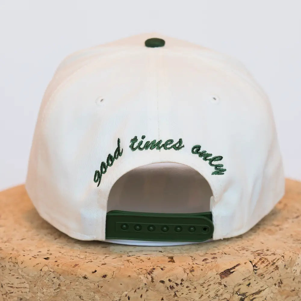 White baseball cap with green embroidered text reading ’good times only’ and a matching green adjustable strap.