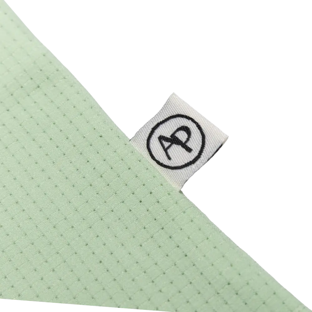 Light green perforated fabric with a white woven label featuring a black circular logo.