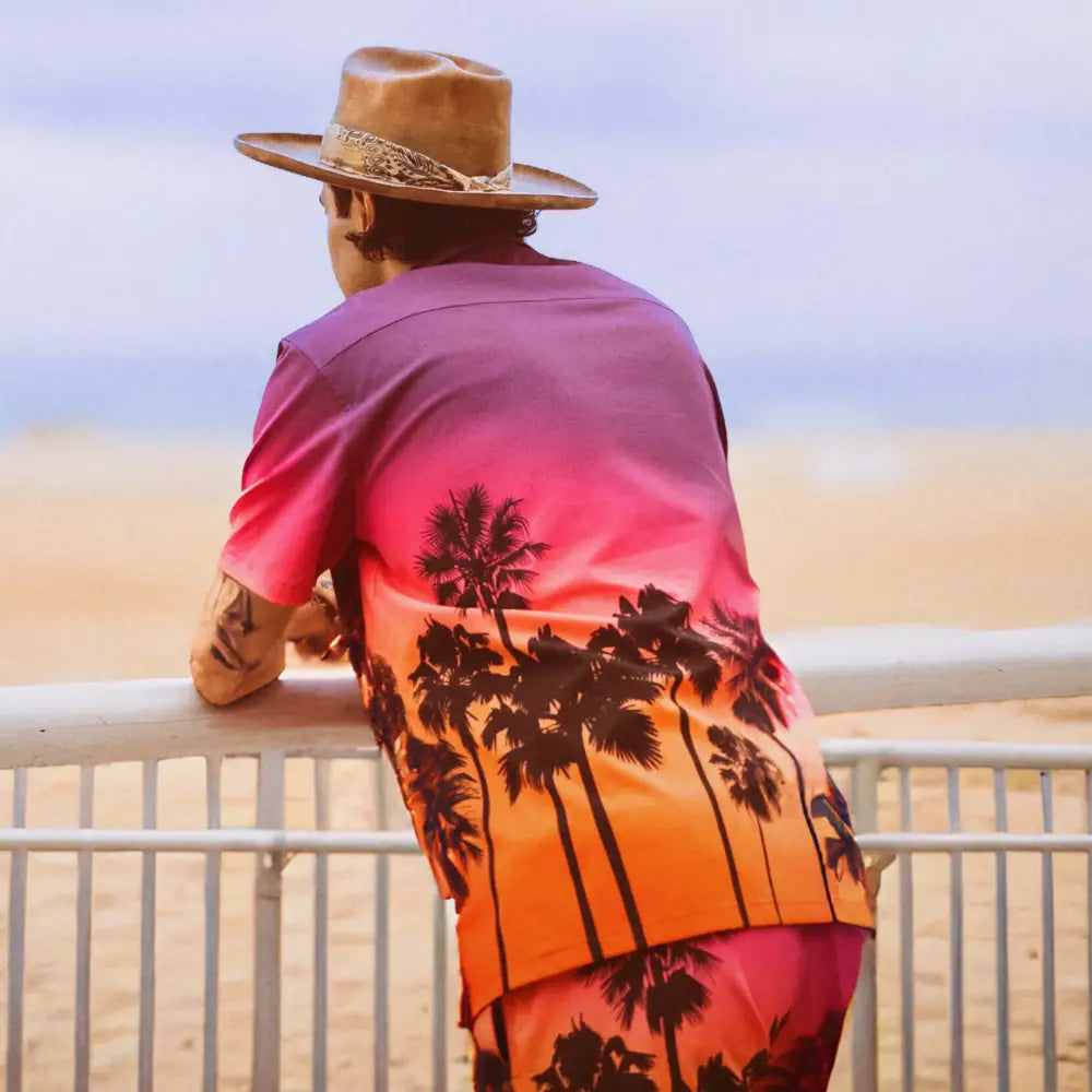 A vibrant gradient hawaiian shirt with black palm tree silhouettes, transitioning from pink to orange.